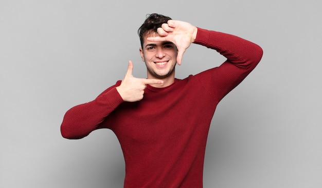 Jeune homme se sentant heureux, sympathique et positif, souriant et faisant un portrait ou un cadre photo avec les mains