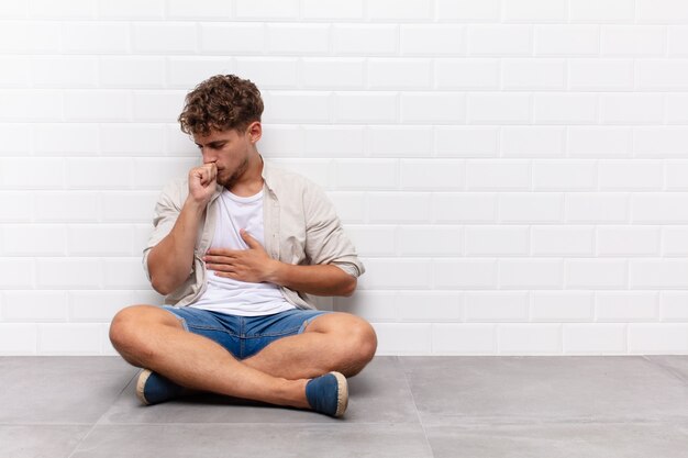 Jeune homme se sentant malade avec un mal de gorge et des symptômes de grippe, toussant avec la bouche cône