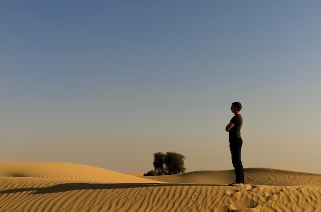 Un jeune homme se tenant dans un désert sur les lumières du coucher du soleil avec une longue ombre