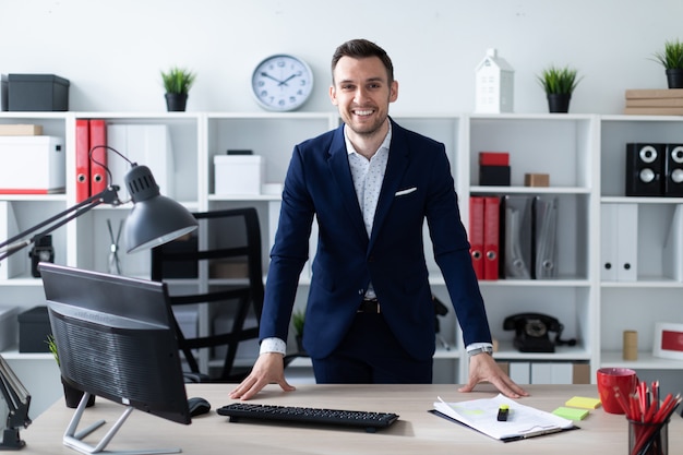 Un jeune homme se tient dans le bureau près de la table et pose ses mains sur lui.