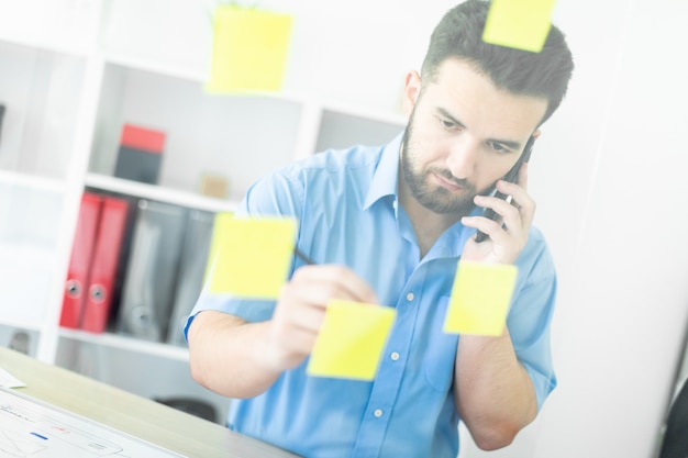 Un jeune homme se tient dans le bureau près d'un tableau transparent avec des autocollants.