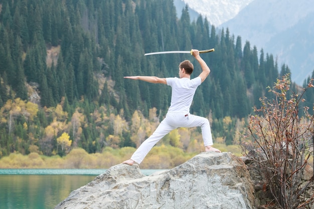 Un jeune homme se tient debout sur une grosse pierre et tient une épée japonaise dans ses mains.