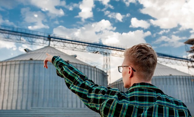 un jeune homme se tient près d'un entrepôt de céréales et montre avec sa main