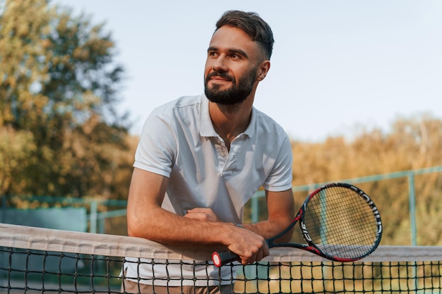 Photo un jeune homme se tient avec une raquette dans les mains sur le court de tennis en plein jour.