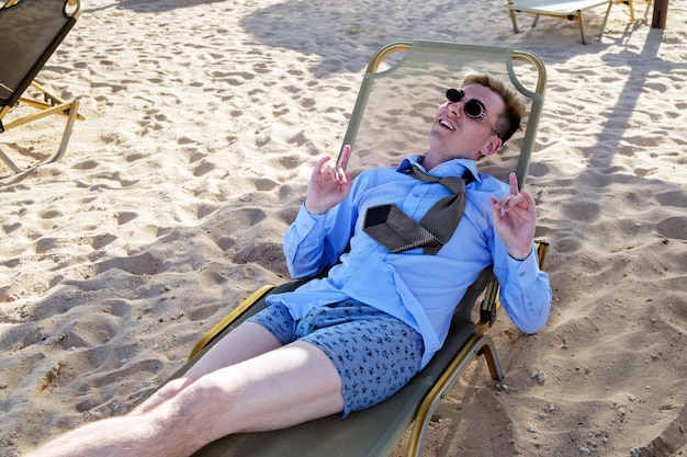 Jeune homme se trouve sur une chaise longue au milieu de la plage dans une chemise cravate et caleçon montre han