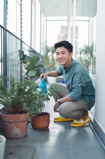 Jeune homme séduisant sur le balcon de l'appartement arrosage des plantes en boîte de l'arrosoir bleu