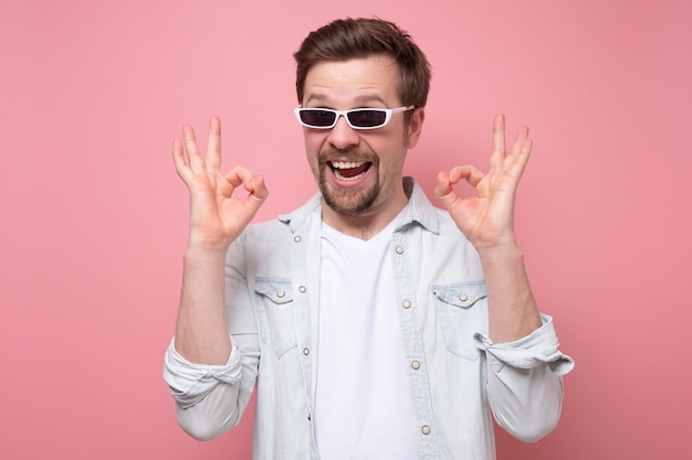Jeune homme séduisant positif dans des lunettes d'été montrant l'approbation OK de votre choix