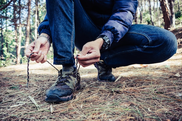 Jeune homme sur un sentier de randonnée lie le lacet sur sa chaussure de marche, photo gros plan