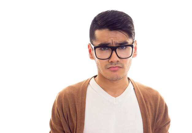 Jeune homme sérieux aux cheveux noirs en T-shirt blanc cardigan marron avec des lunettes noires en studio