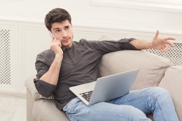 Jeune homme sérieux avec des gadgets. Consultant indépendant sur mobile tout en travaillant sur un ordinateur portable, espace de copie