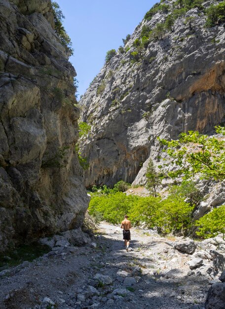 Un jeune homme en short et une casquette de baseball se promène dans une gorge de montagne en Grèce