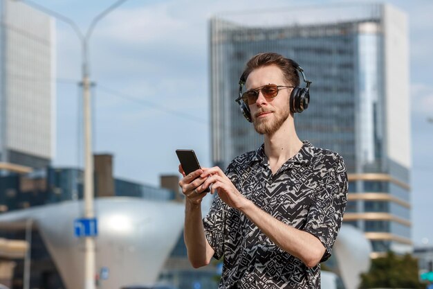 Un jeune homme avec un smartphone dans des écouteurs et des lunettes de soleil