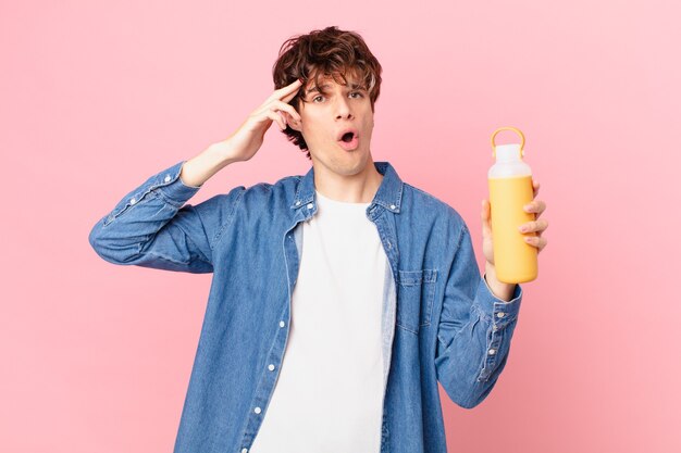 Jeune homme avec un smoothie semblant heureux, étonné et surpris