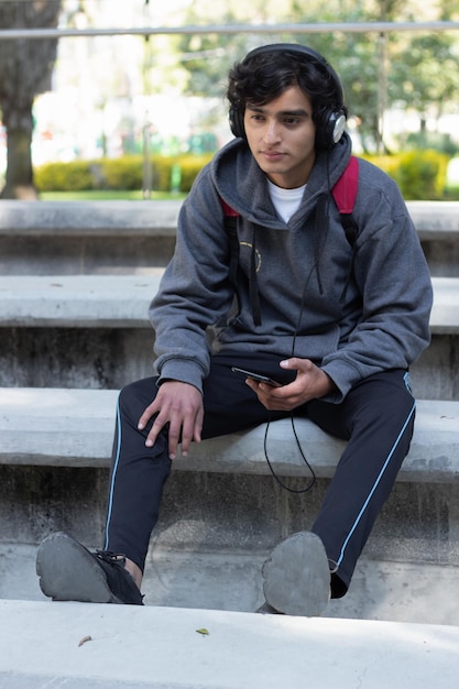 Jeune homme solitaire et triste écoutant de la musique dans le parc avec ses écouteurs, son visage est mélancolique et déprimé.