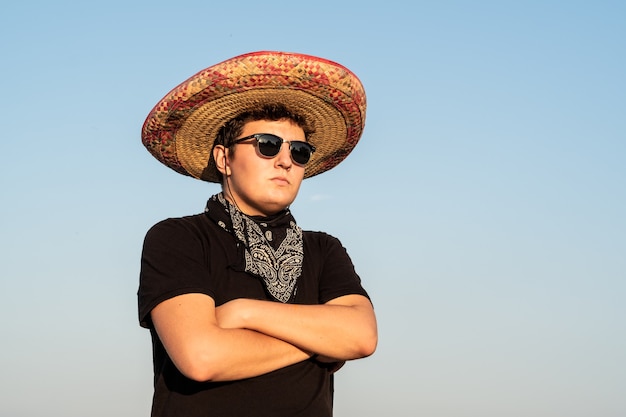 Jeune homme en sombrero et lunettes de soleil en fond de ciel clair. Mexique concept de fête de l'indépendance de l'homme portant un chapeau mexicain national et un bandana de style occidental