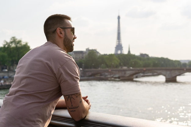 Jeune homme avec son dos contre un pont au premier plan surplombant la Tour Eiffel et la Seine