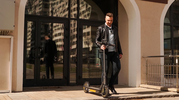 Un Jeune Homme Sort De L'entrée De Sa Maison Et Tient Un Scooter électrique à La Main. Il Va Faire Du Scooter. Journée Ensoleillée.