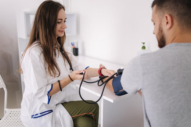 Jeune homme souffrant d'hypertension artérielle femme médecin à l'aide d'un sphygmomanomètre avec contrôle du stéthoscope