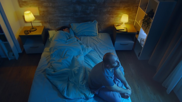 Jeune homme souffrant d'insomnie pendant que sa femme dort. Clair de lune.