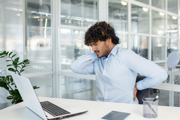 Un jeune homme souffre de maux de dos alors qu'il travaille à son bureau.