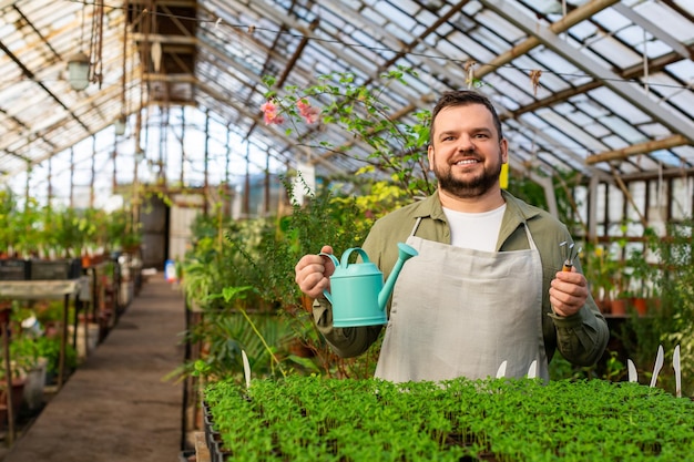 Un jeune homme souriant avec arrosoir dans une serre