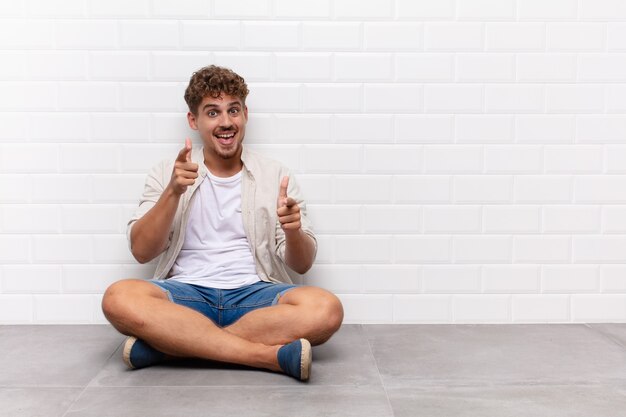 Jeune homme souriant avec une attitude positive, réussie et heureuse, pointant vers la caméra, faisant signe des armes à feu avec les mains