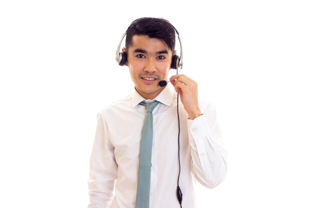 Jeune homme souriant aux cheveux noirs en chemise blanche avec cravate bleue à l'aide d'un casque en studio