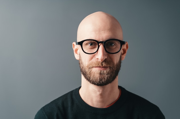 Jeune homme souriant avec barbe et lunettes sur fond gris studio