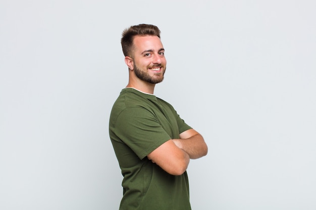 Jeune homme souriant avec les bras croisés et une expression heureuse, confiante et satisfaite, vue latérale