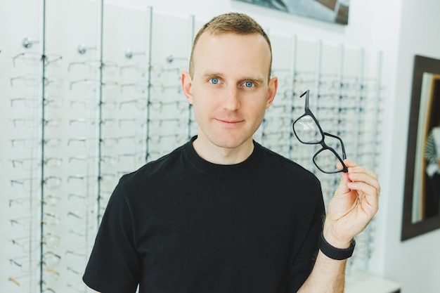 Un jeune homme souriant choisit des lunettes pour la correction de la vision dans un salon d'ophtalmologie Lunettes pour la correction de la vision