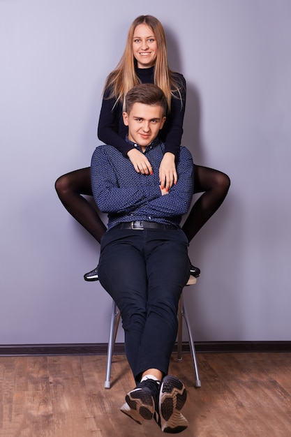 Jeune homme souriant et femme posant pour le photographe assis ensemble sur la même chaise dans le salon.