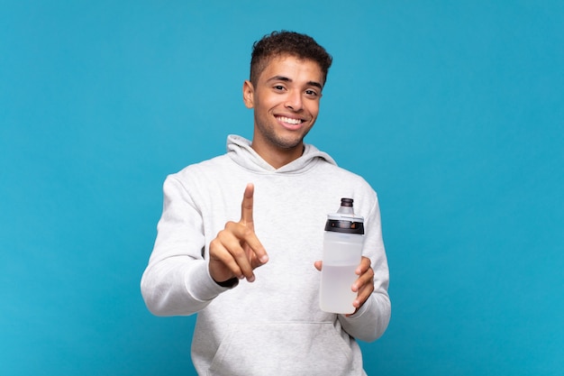 Jeune homme souriant fièrement et avec confiance faisant triomphalement la pose numéro un, se sentant comme un leader. notion de sport