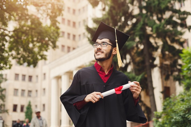 Jeune homme souriant le jour de sa remise des diplômes à l'université titulaire d'un diplôme, copiez l'espace. Concept d'éducation, de qualification et de robe.