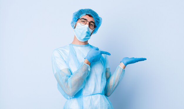 Jeune homme souriant joyeusement et pointant pour copier l'espace sur la paume sur le côté, montrant ou annonçant un objet. concept de coronavirus