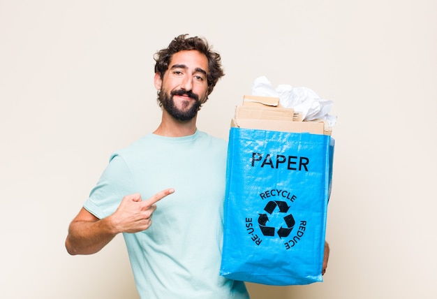 Jeune homme souriant joyeusement et pointant vers le côté et vers le haut avec les deux mains montrant l'objet dans l'espace de copie