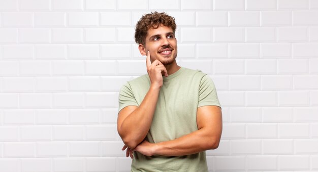 Jeune homme souriant joyeusement et rêvassant ou doutant isolé