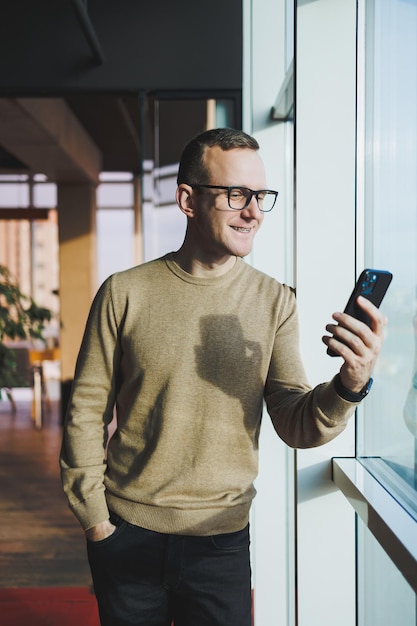 Un jeune homme souriant à lunettes sourit et parle au téléphone sur un téléphone portable tout en se relaxant au bureau Un jeune pigiste travaille à distance