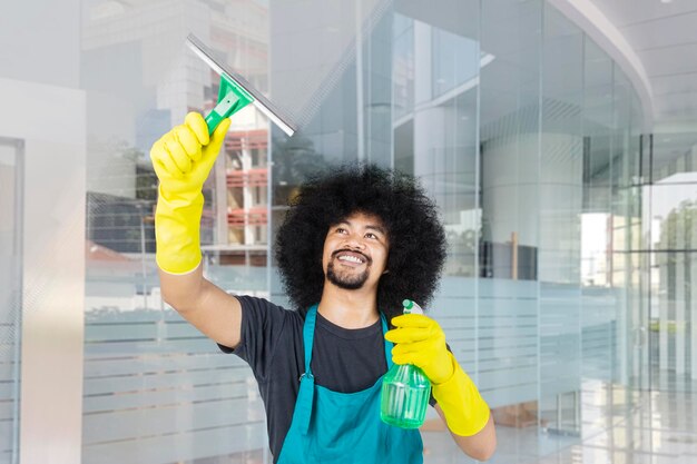 Photo un jeune homme souriant nettoie la fenêtre dans son bureau.