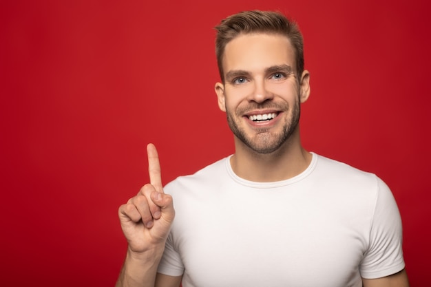 jeune homme souriant pointant avec le doigt vers le haut isolé sur rouge