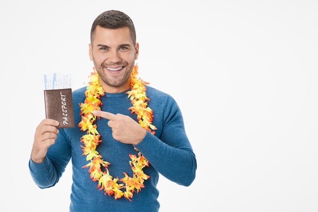 Jeune homme souriant pointant sur un passeport avec des billets posant isolé sur fond de mur blanc