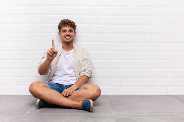 Jeune homme souriant et à la recherche amicale, montrant le numéro un ou d'abord avec la main en avant