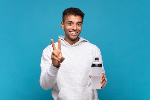 Jeune homme souriant et regardant heureux, insouciant et positif, faisant des gestes de victoire ou de paix d'une seule main. concept de sport