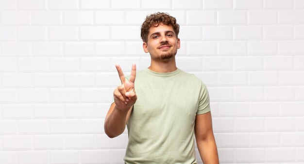 Jeune homme souriant et à la sympathique, montrant le numéro deux ou seconde avec la main en avant, compte à rebours