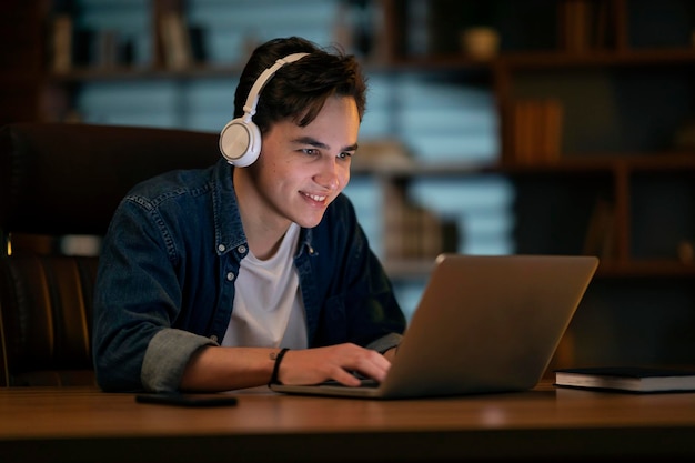 Jeune homme souriant travaillant sur un ordinateur portable tard dans la nuit