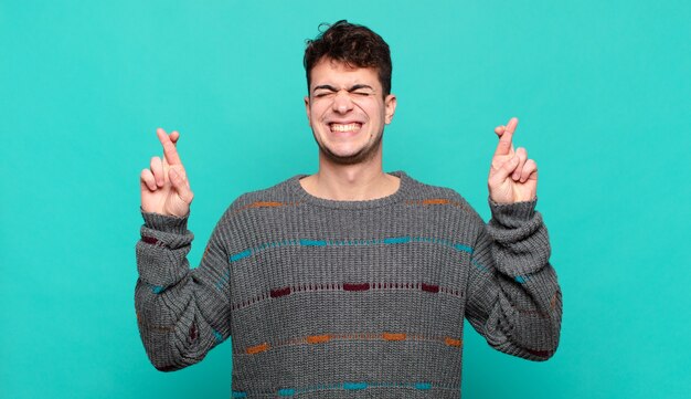 Jeune homme souriant et traversant anxieusement les deux doigts, se sentant inquiet et souhaitant ou espérant avoir de la chance