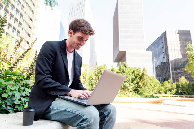 Un jeune homme souriant utilisant un ordinateur portable assis sur un banc