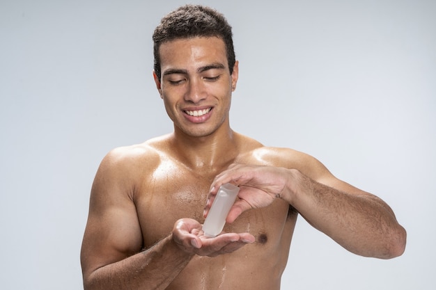 Jeune homme souriant versant une lotion après-rasage sur sa main