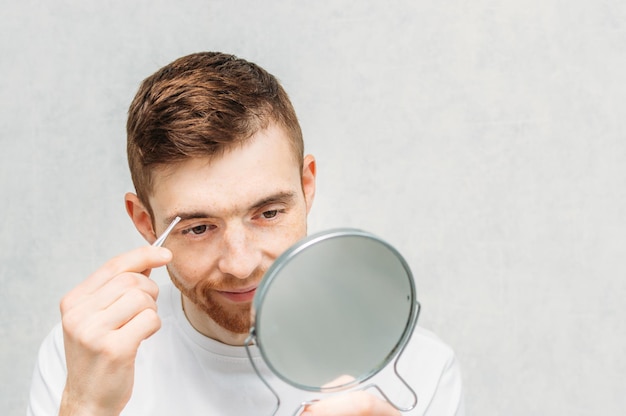 Le jeune homme avec un sourire sur son visage s'épile les sourcils.