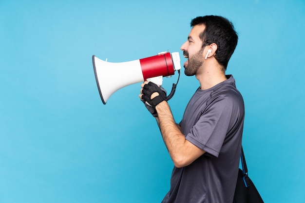 Jeune homme de sport avec barbe sur bleu isolé criant à travers un mégaphone