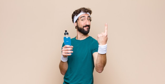 Jeune homme de sport avec une bouteille de boisson énergisante contre un mur plat